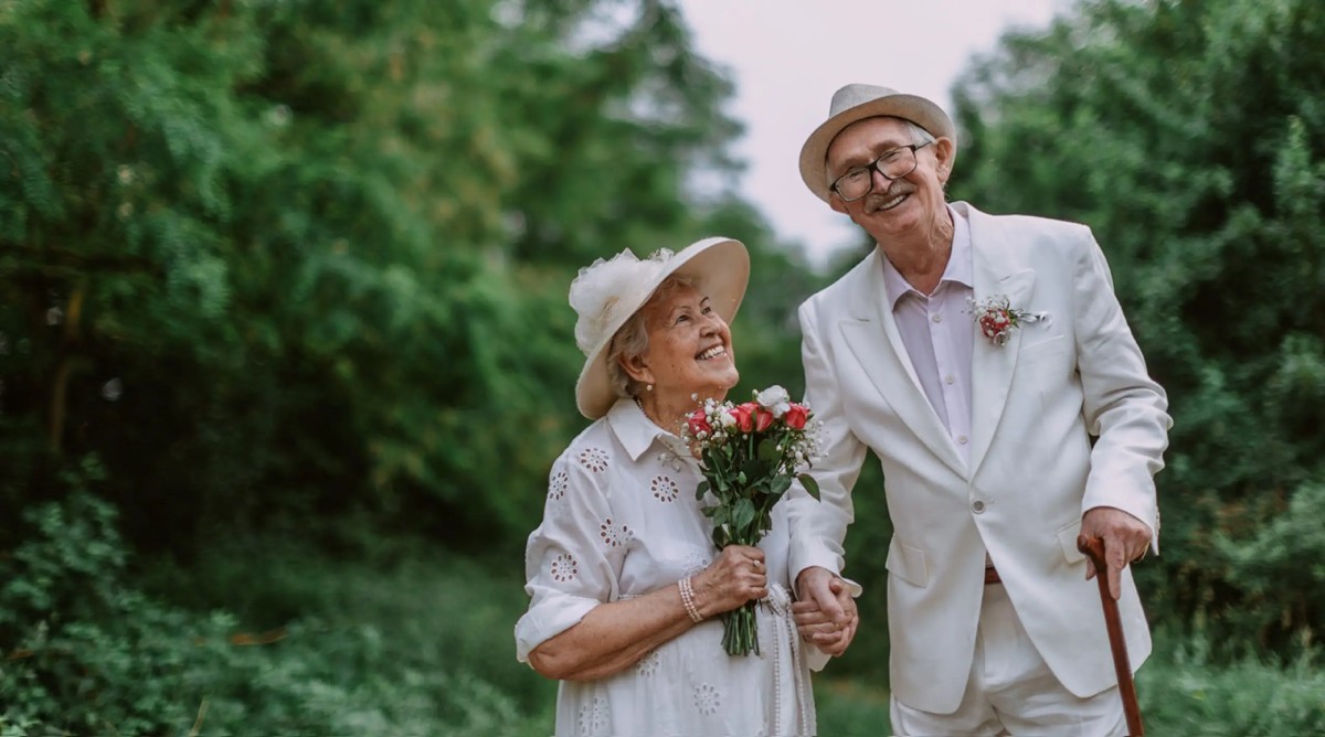 Un couple âgé, souriant et marchant main dans la main, tenant un bouquet de fleurs. Une belle illustration des noces d’or et de l’amour qui dure à travers le temps.